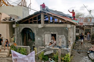 Tarp distributions take place in different barangays in central Palo, a city hard-hit by Typhoon Haiyan / Yolanda that devastated the central Philippines in November 2013. A mix of CRS staff and volunteers helped the distributions run smoothly and ensured that any problems could be dealt with using a structured system. Here, a tarp goes up on a damaged home as the distribution is taking place. (Photo by Jennifer Hardy/CRS)